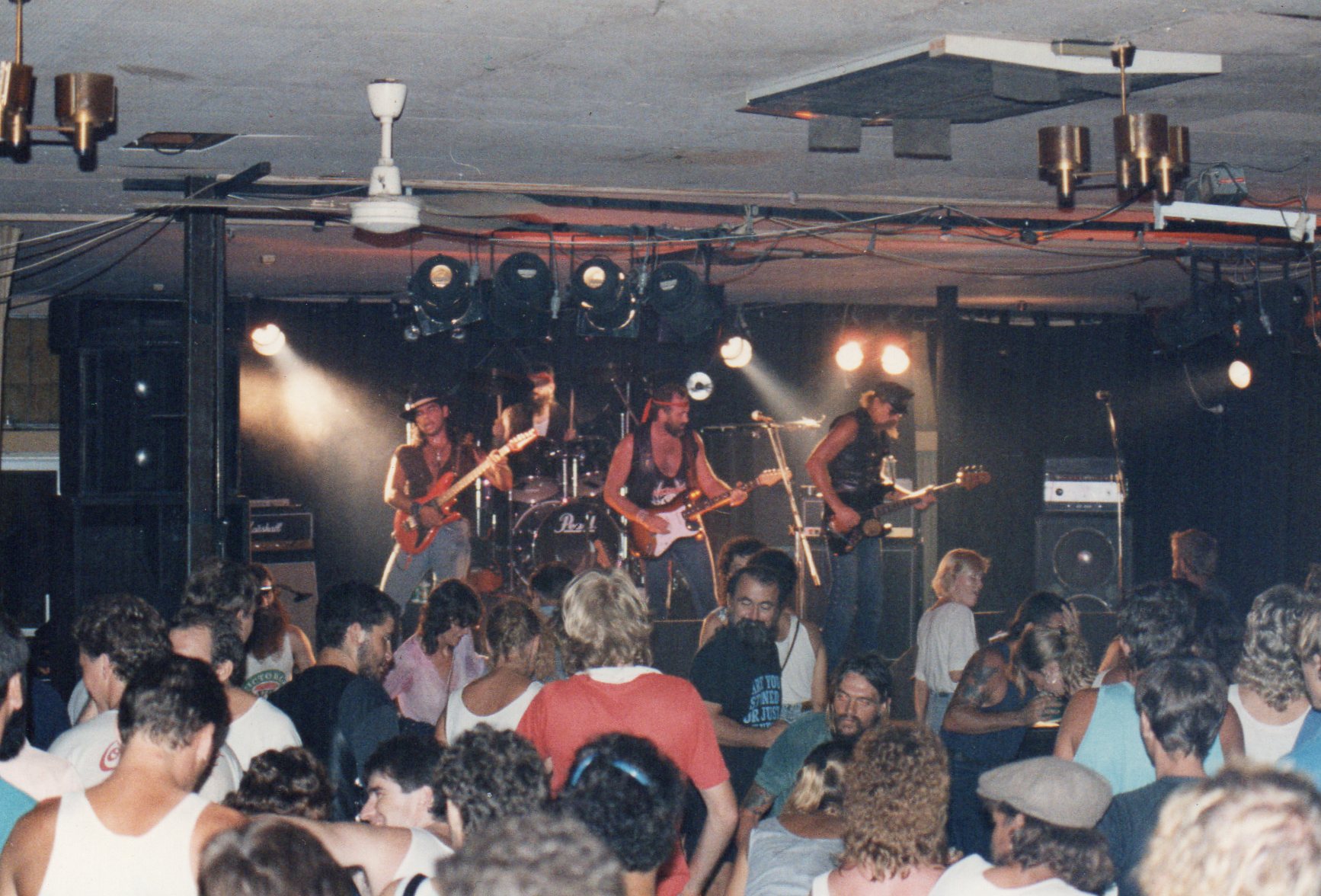 Bandanna playing to a full pub band room, seen from the back of the crowd under red and white stage lights